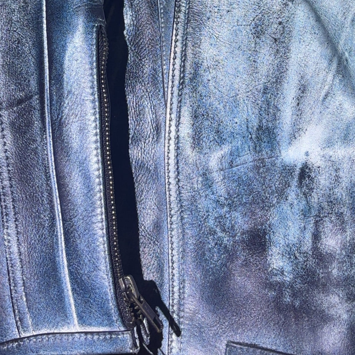 R4RE CHROMITE jacket — center front zip detail, chrome-treated cowhide leather surface showing gunmetal to silver tonal variation, topstitched storm flap, YKK zipper hardware against distressed leather face
