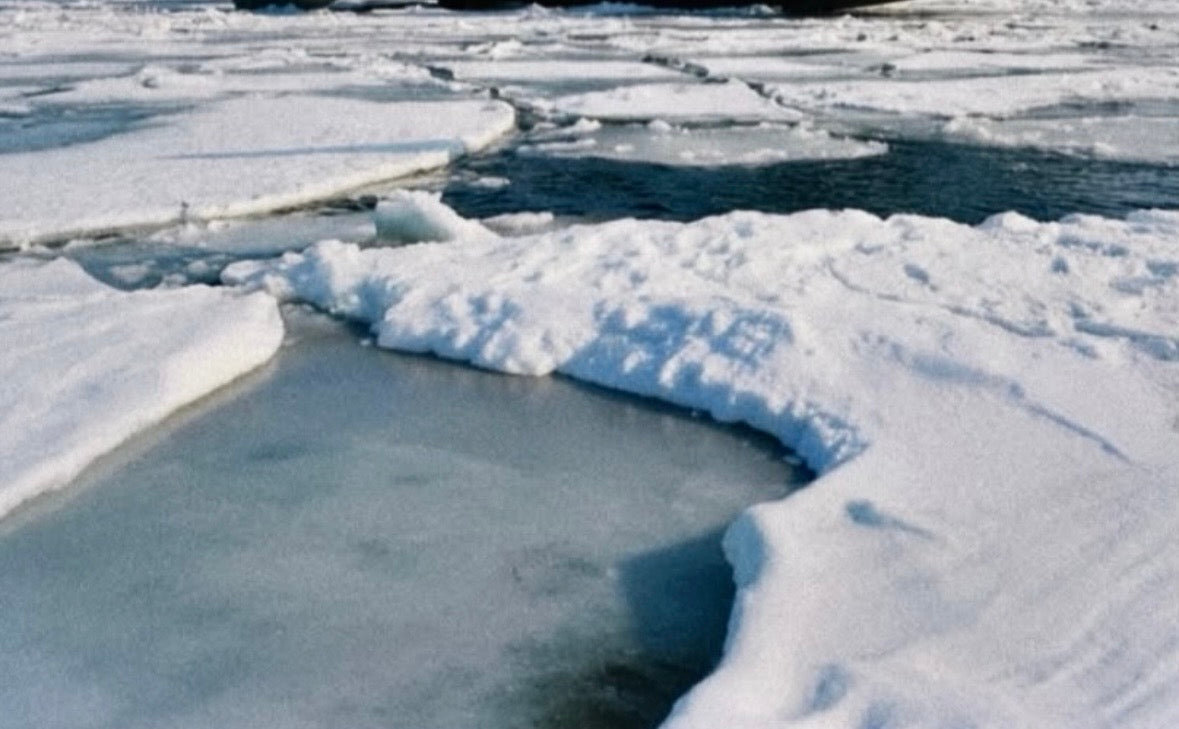 A natural winter landscape showing broken ice, snow, and dark water channels.